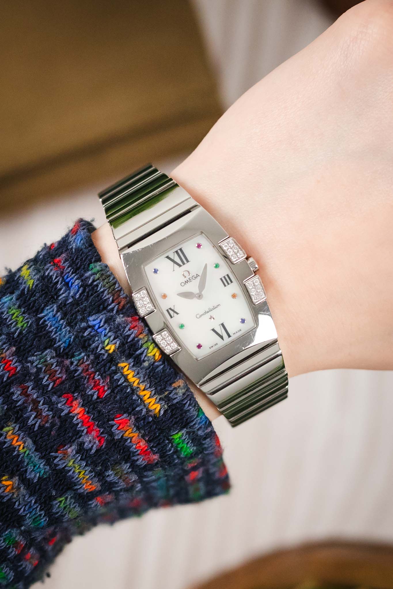 A lifestyle shot of the watch being worn on a wrist, paired with a dark, multi-colored knit sweater, showing the elegant fit of the rectangular case.