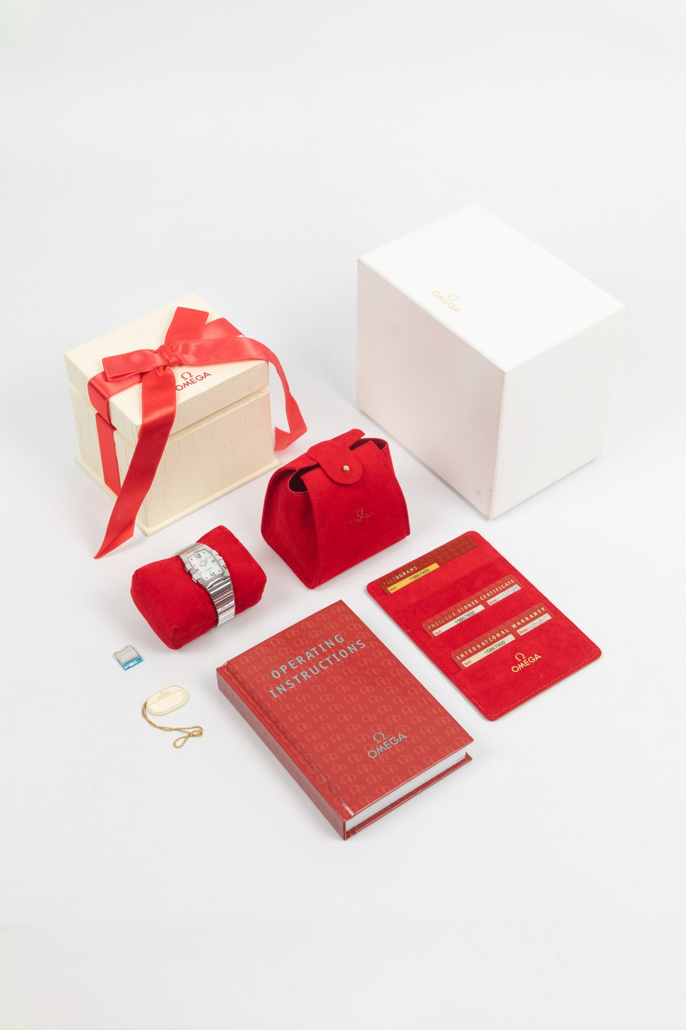 A wide-angle shot of the complete "full set," featuring the watch on a red velvet cushion, its original cream-colored box with a red ribbon, a red travel pouch, various warranty and gemstone certificates, and the red operating instructions book.