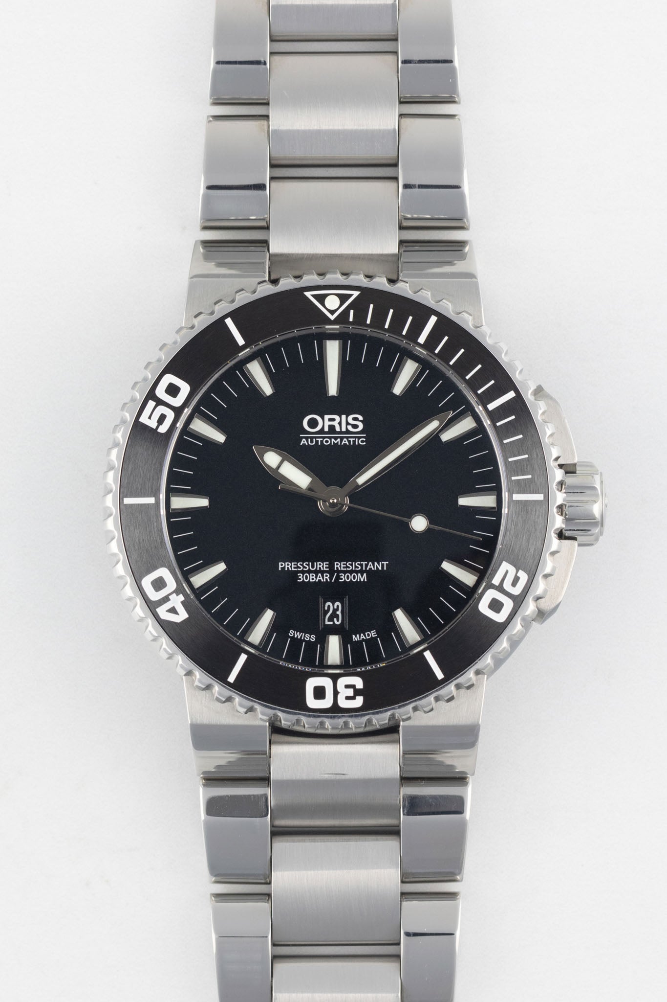 A direct, front-facing studio photograph of an Oris Aquis Date watch with a black dial, white date window at 6 o'clock, and an integrated stainless steel bracelet on a white background.