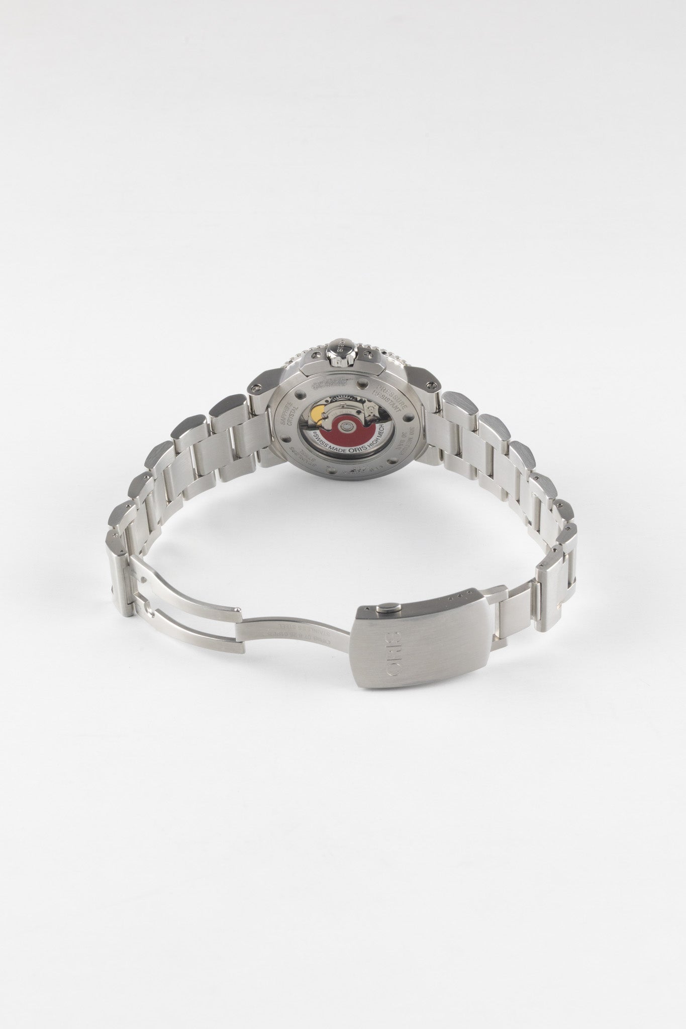 An angled view of the open stainless steel bracelet and case back of an Oris Aquis Date, showcasing the exhibition window and the signature red Oris automatic rotor.