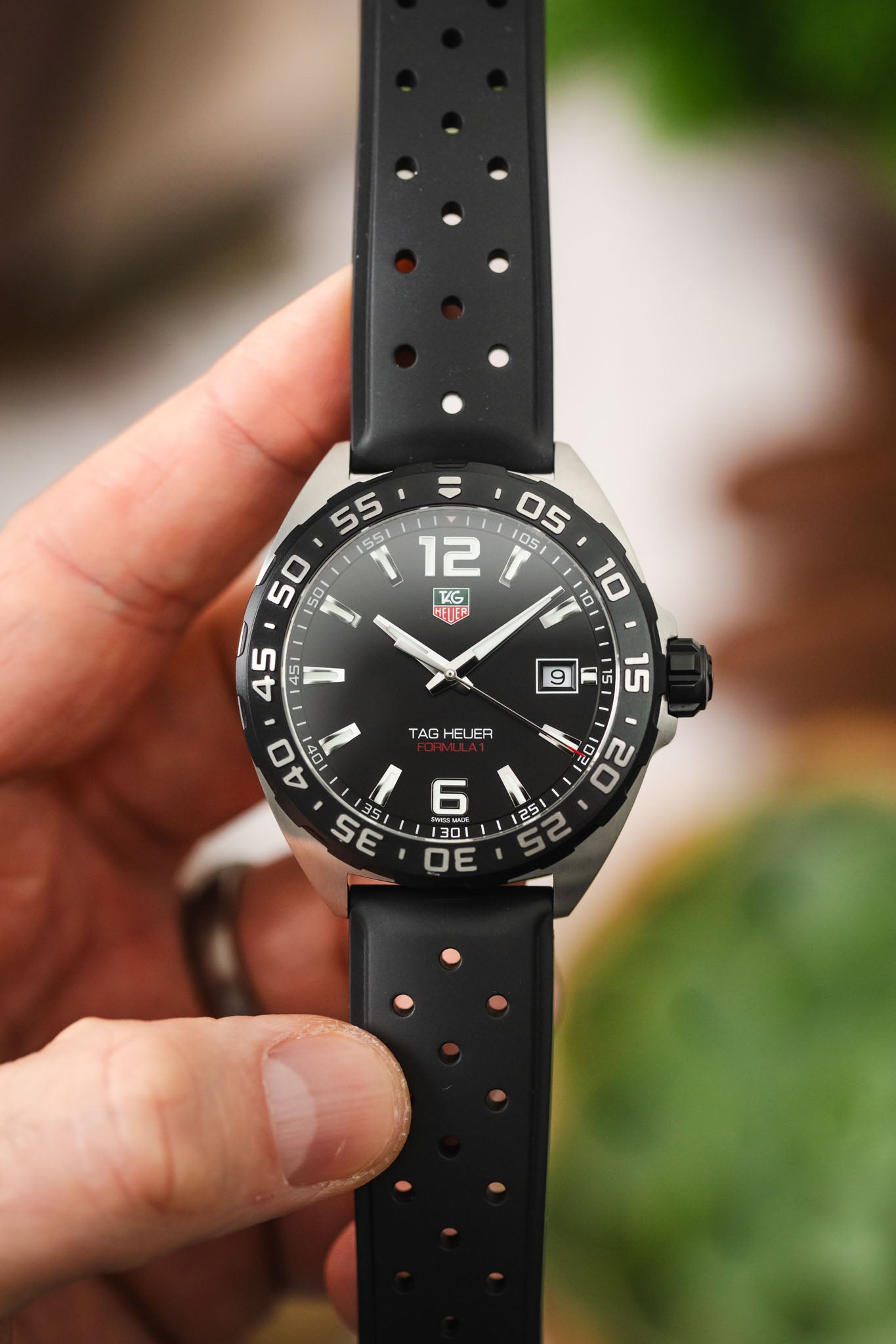 A close-up hand-held shot focusing on the watch face, showing the luminous hands, date window at 3 o'clock, and the "12" and "6" Arabic numerals.