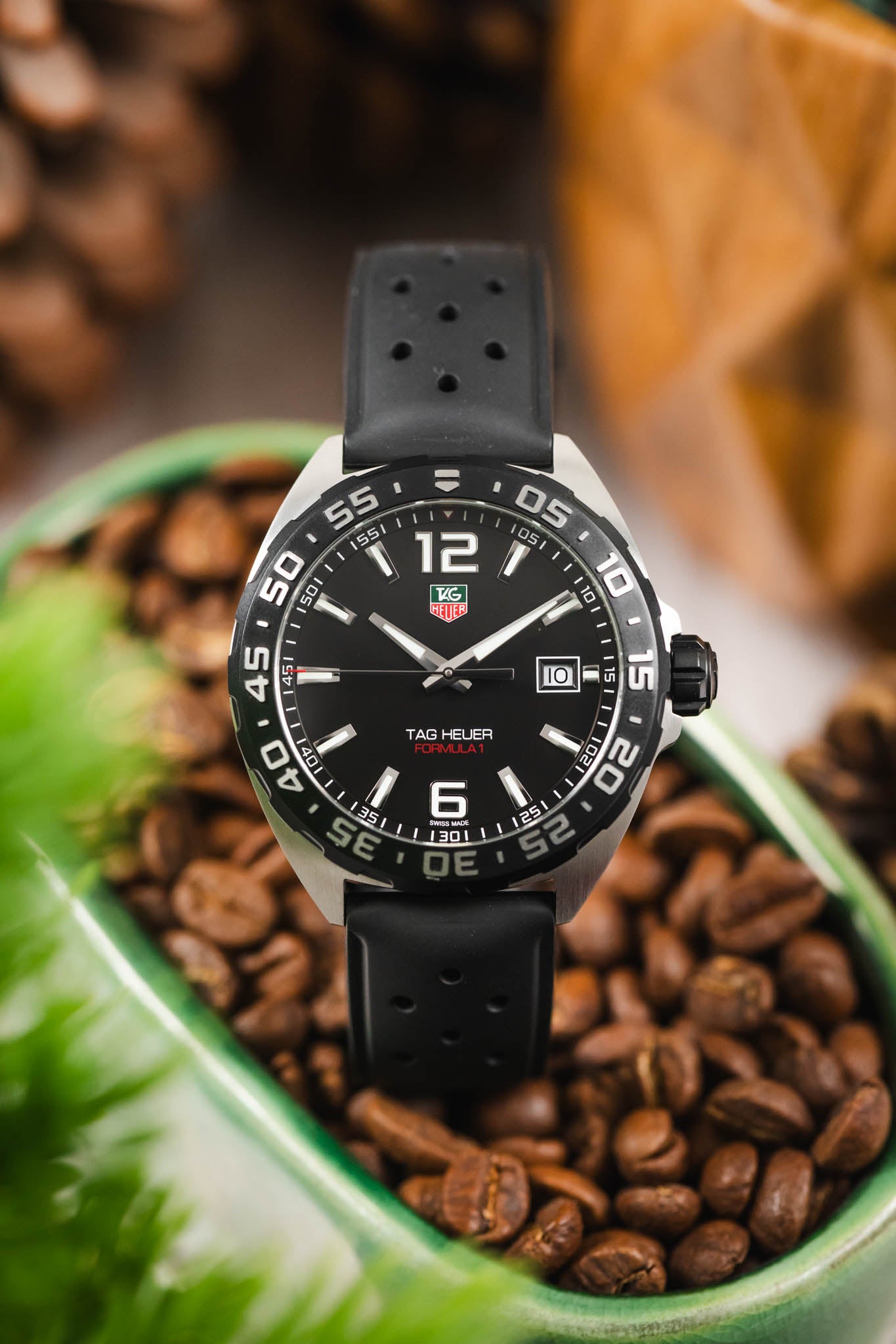 A creative shot of the TAG Heuer watch positioned upright inside a green bowl filled with roasted coffee beans.