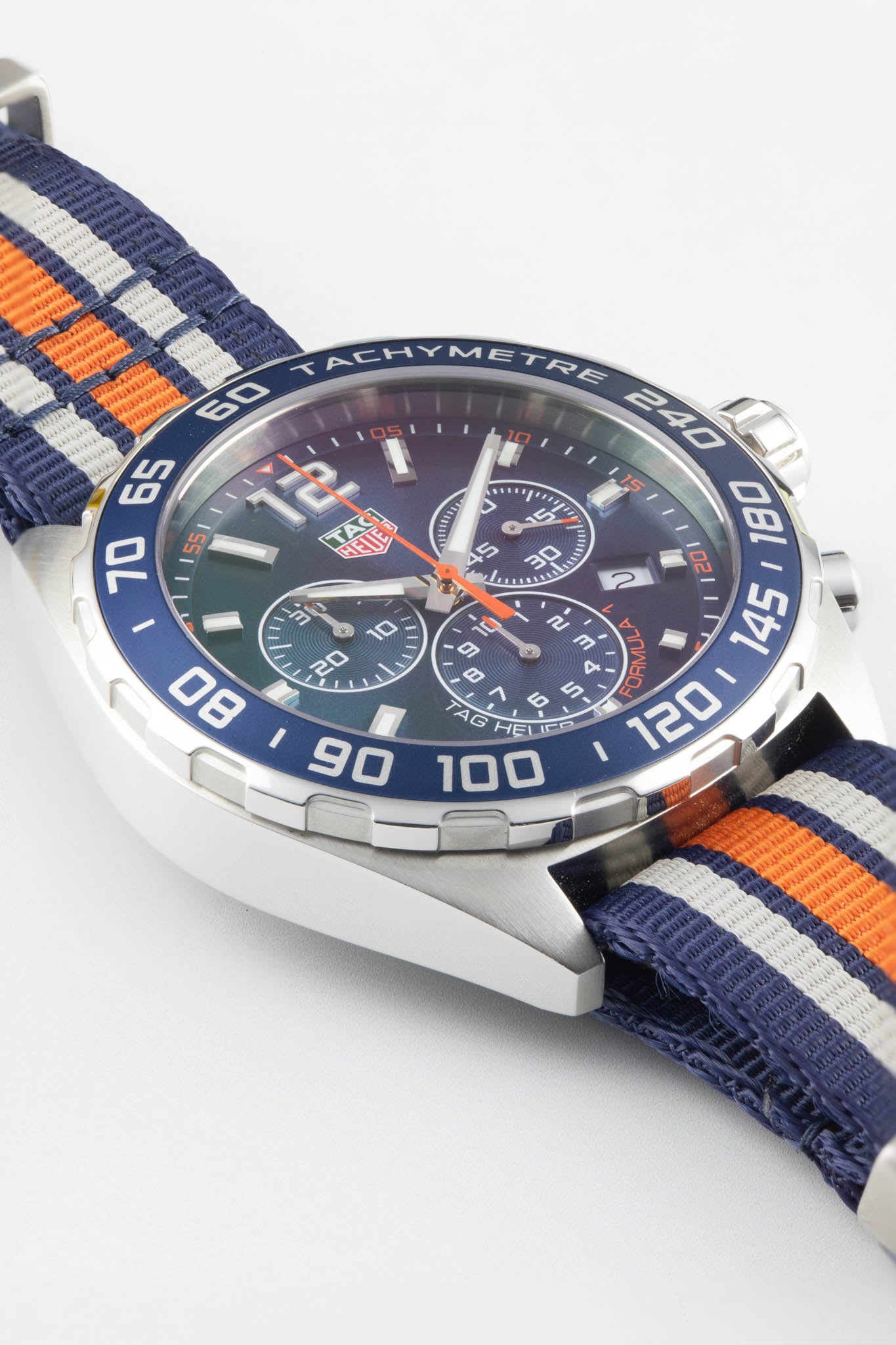 A macro-angled shot focusing on the texture of the blue bezel and the orange accents on the chronograph hands and sub-dials.