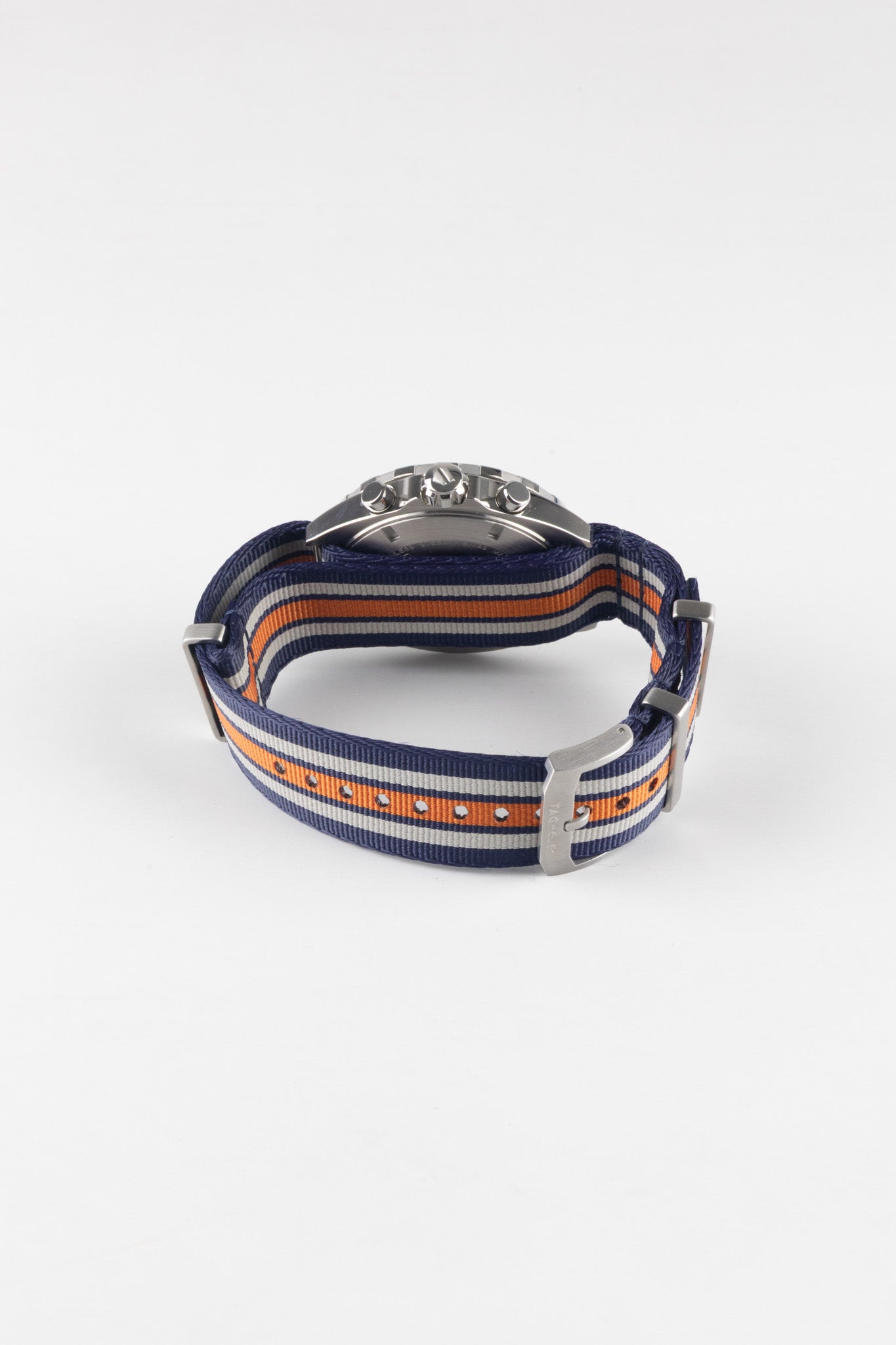 A view of the watch from the back, showing how the blue and orange striped fabric strap threads through the lugs and the engraved steel pin buckle.