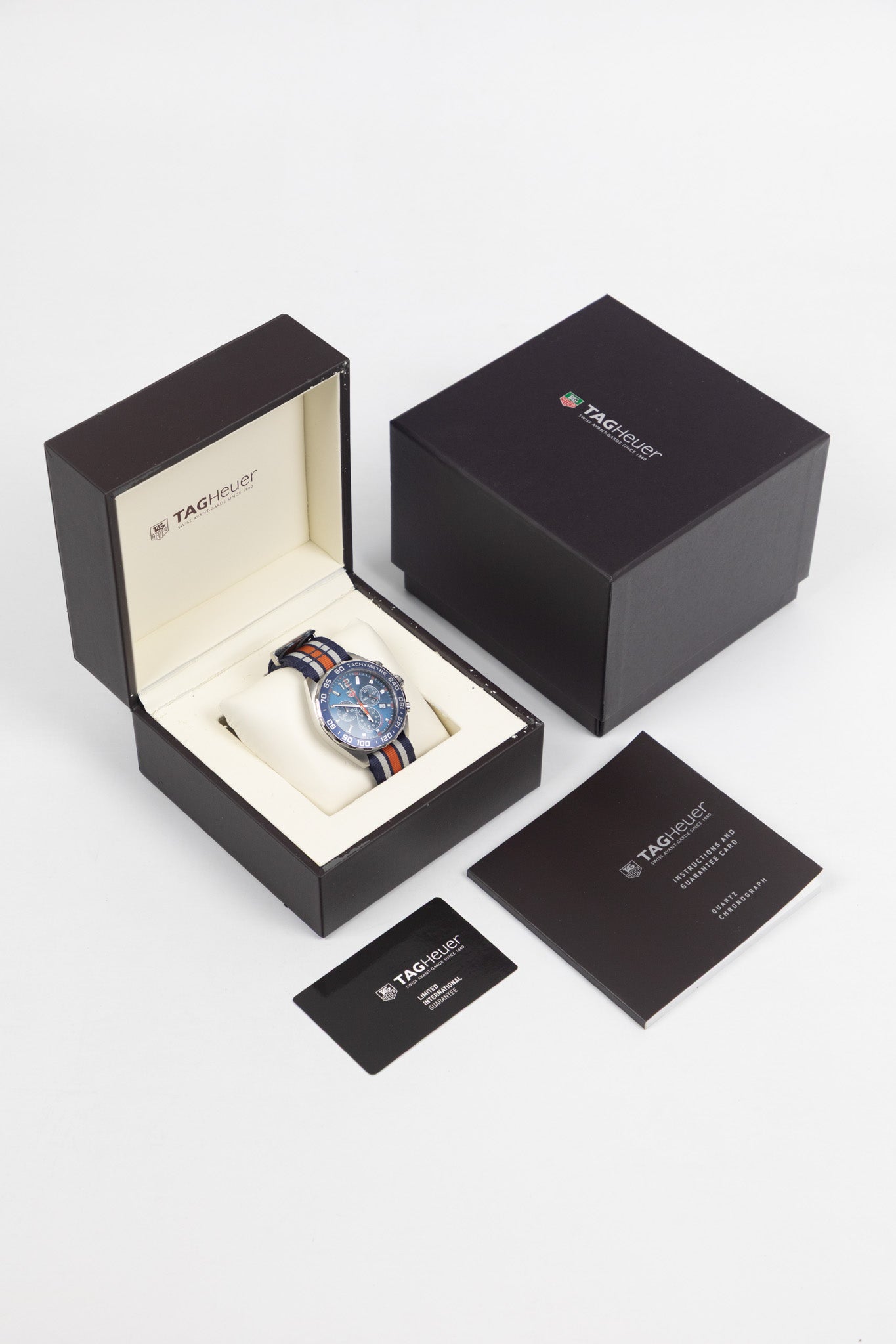 A "full set" display including the watch on a cushion inside a brown TAG Heuer box, accompanied by the outer box, instruction manual, and a "Limited International Guarantee" card.